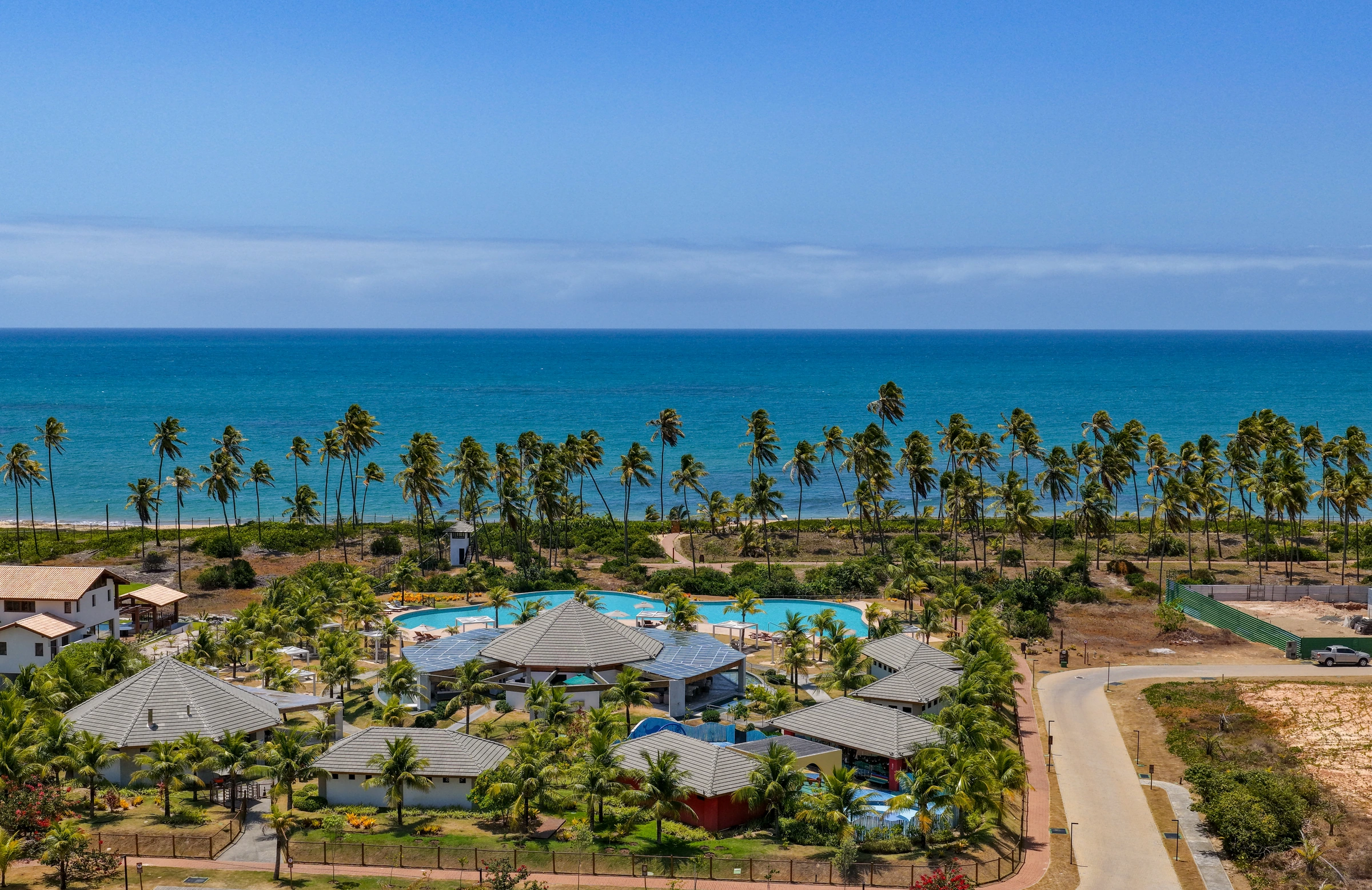 Vista aérea aberta do Clube da Praia, com construções, piscina, coqueiros e mar.