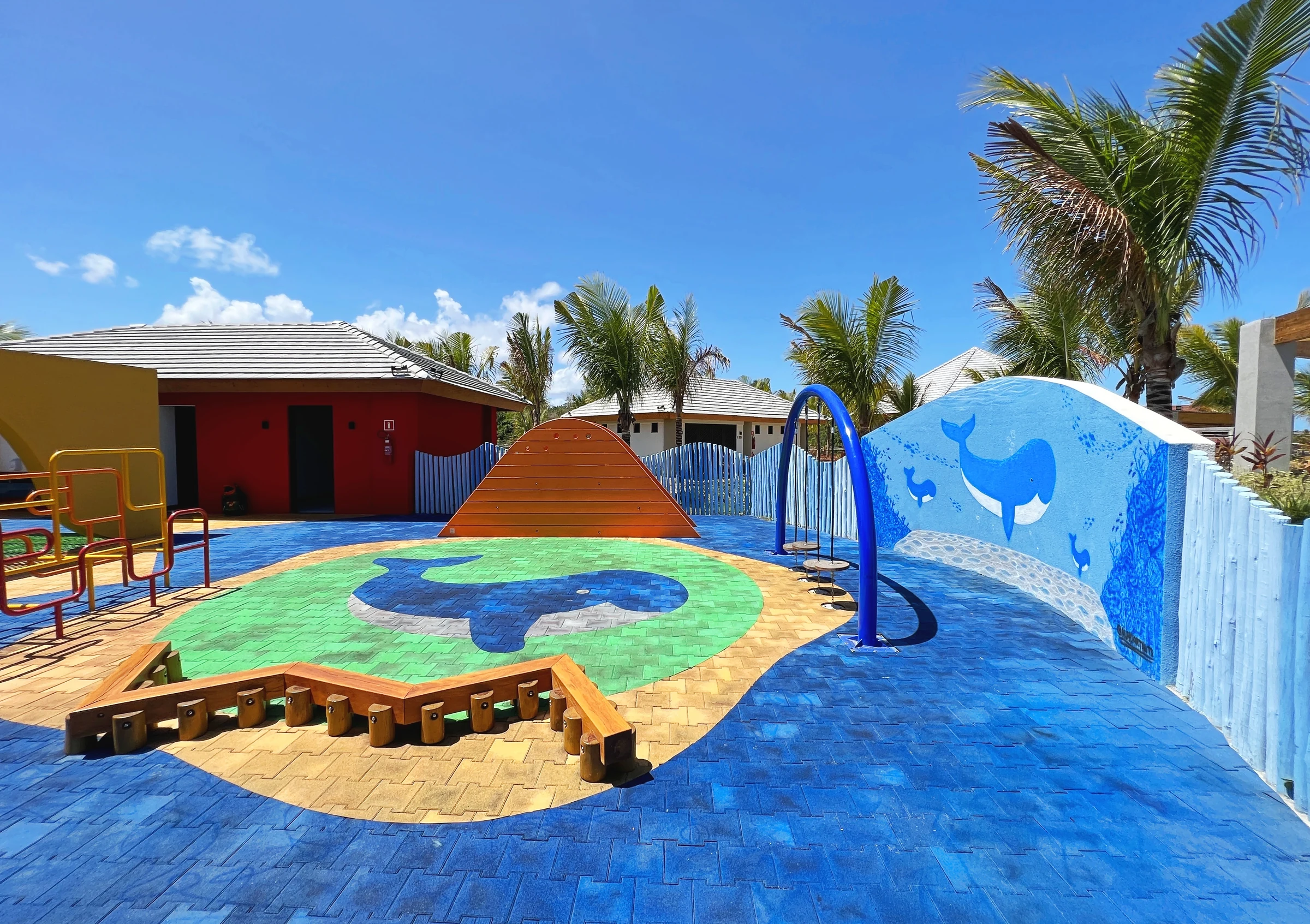 Playground colorido com pontes, estruturas de brincar e piso temático.